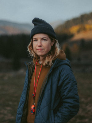 Person wearing a blue jacket and black beanie standing in a natural landscape.