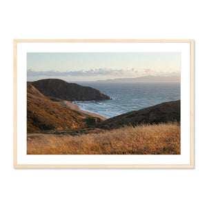 Windswept Coastal Vista framed photography print showing a serene coastal landscape with rolling hills, golden grasses, and ocean waves under a soft morning sky.