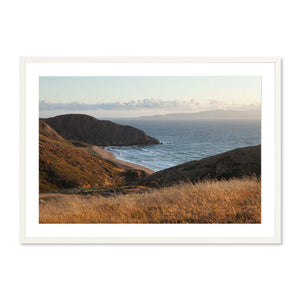 Windswept Coastal Vista featuring a serene landscape of golden grassy hills and rugged cliffs overlooking a calm ocean under a soft pastel sky, framed as fine art photography print.