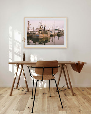 Wooden desk with chair in a room with a large framed photograph of a marina on the wall.