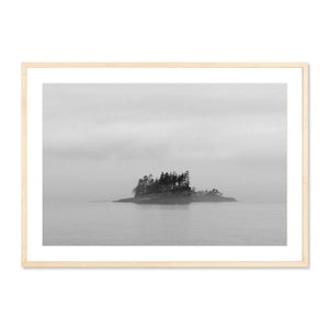 Framed black and white photography print of a solitary misty island with tall trees rising from calm water, titled Inside Passage Island, atmospheric fine art for wall decor.